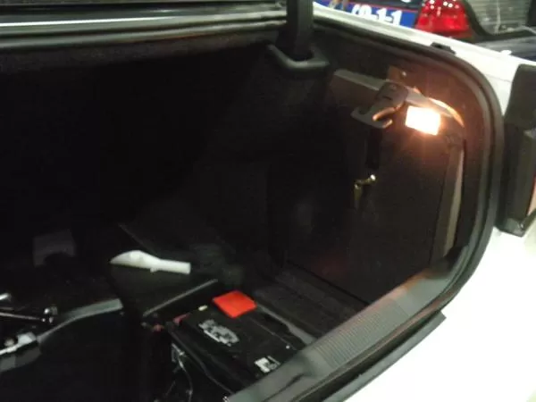 Driver side of a white Charger trunk with the door closed, brass key lock and dome light switched on