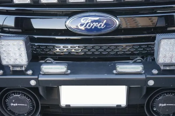 Slim modules mounted on the licence plate bar of a Ford grille between two larger LED lamps