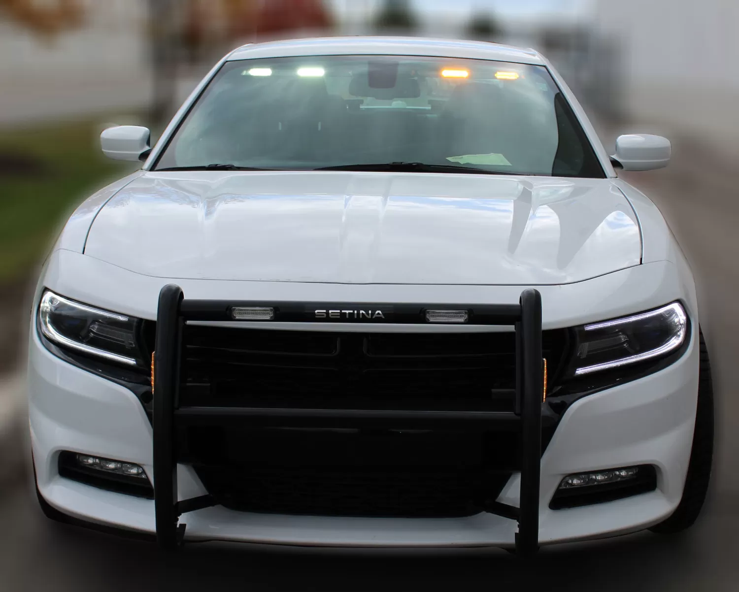 White Dodge Charger with the visor bar lit at the top of the windshield and amber lights in the push bumper