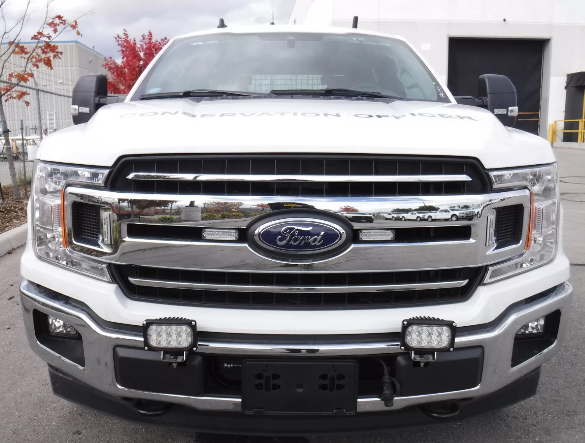 Two of the lamps mounted low on the front bumper of a white Ford pickup lettered CONSERVATION OFFICER