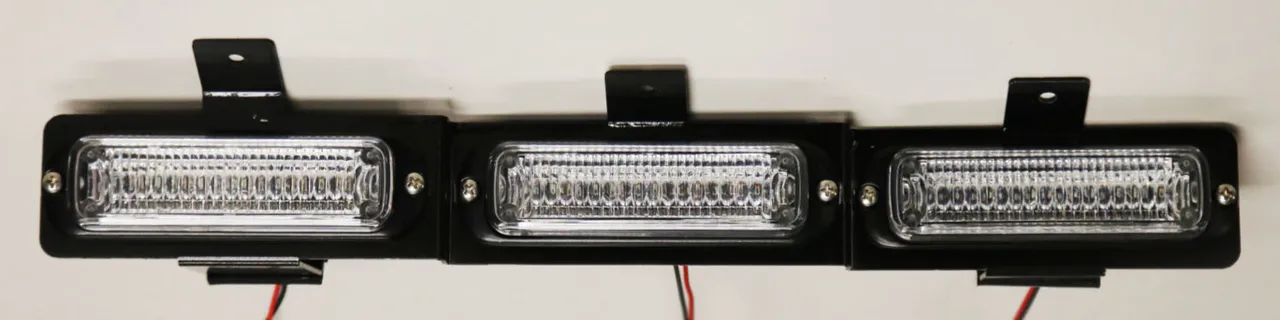 Bare three-module assembly on its black mounting bracket with wiring pigtails, straight-on and unlit