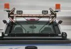 Amber light stick lit on the cab rack of a white truck between two rotating beacons and work lights