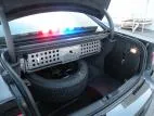 Trunk interior with the perforated aluminum equipment panel mounted above the spare tire, lightbar lit