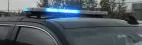 Blue LED modules flashing the full length of the bar on the roof of a black SUV in daylight