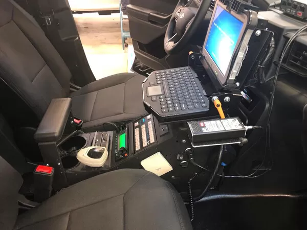 Driver-side view of the installed console carrying a siren controller, radio faceplates and a docked laptop