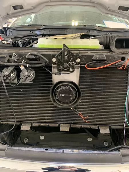 D&R-badged speaker fitted low on the radiator support, photographed under the open hood of a white vehicle